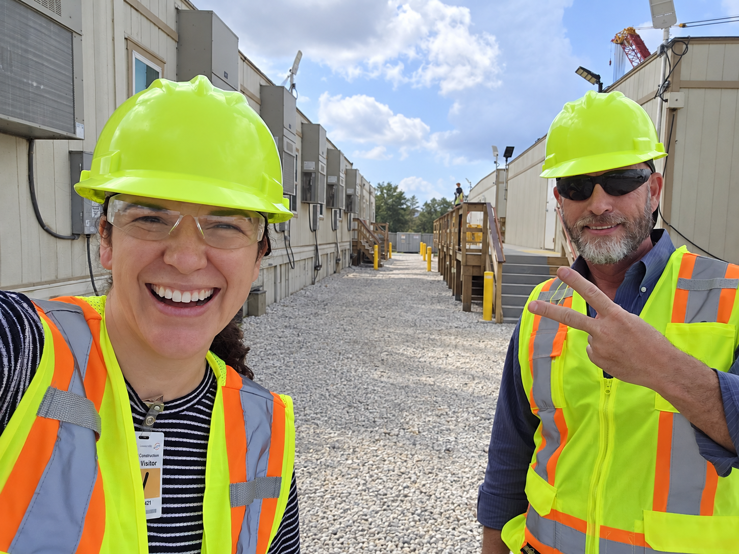 Two people on a site visit, wearing safety vests and plain yellow hardhats.